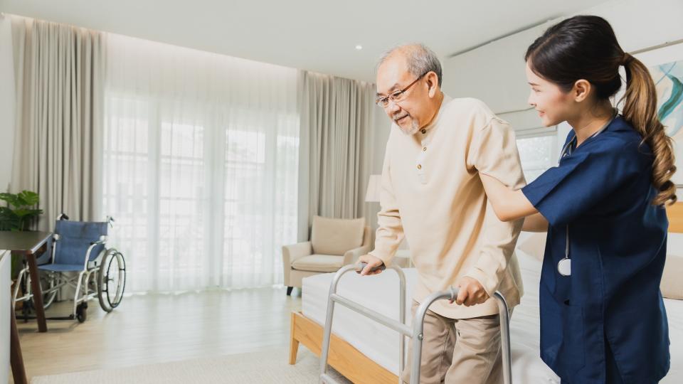 A woman assisting elderly man with walker in bedroom.