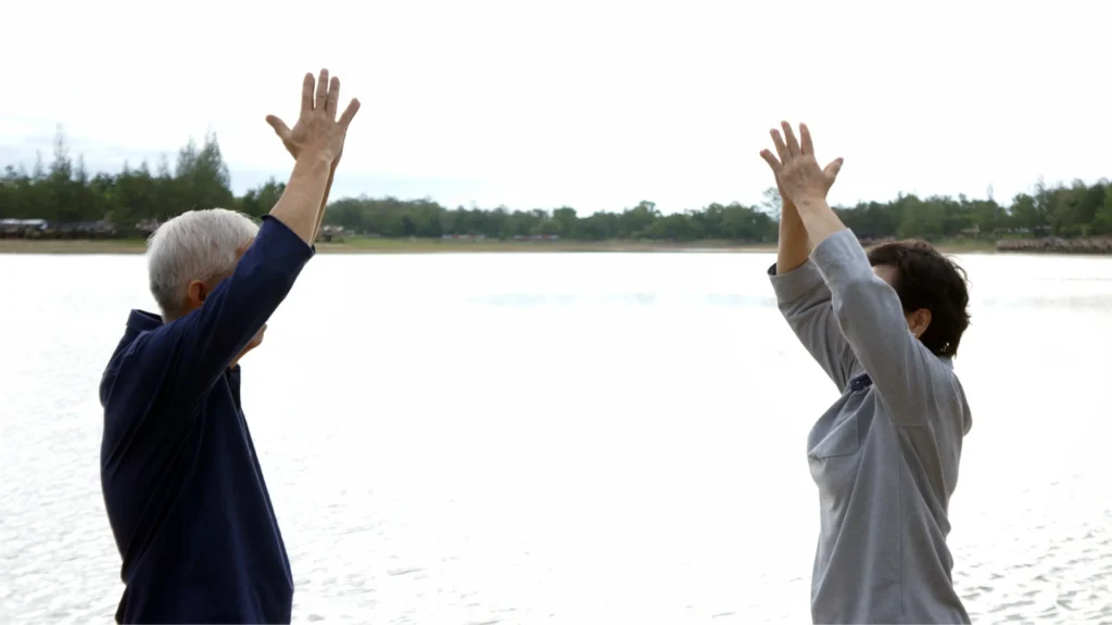 Elderly couple practicing yoga together by a serene lake.