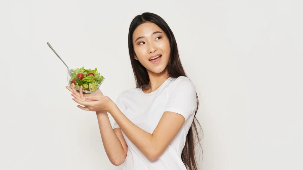 A woman smiling while holding a bowl of fresh salad.