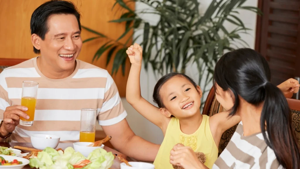 A happy family enjoying a meal together, with a child sitting at the table and a plate of delicious food in front of them.