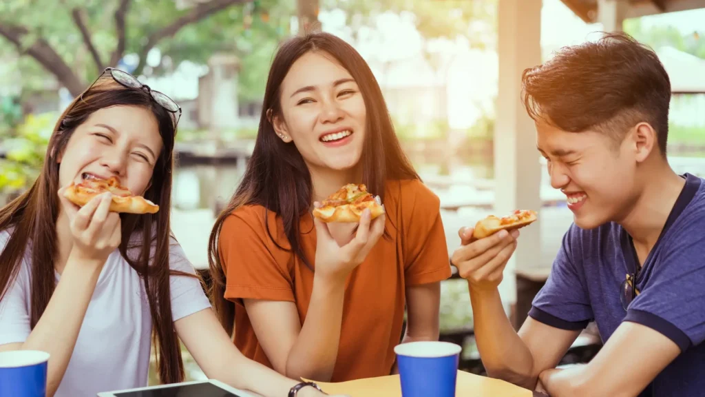 Three young friends enjoying pizza together at a table.
