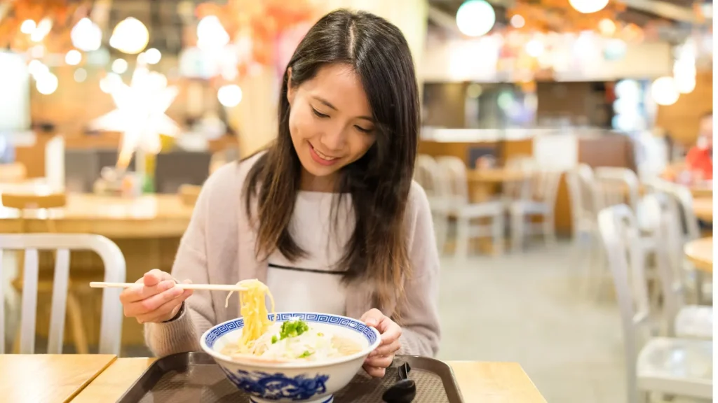 A woman enjoying noodles at a restaurant, savoring every bite with a smile on her face.