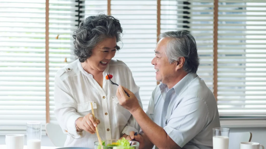 Elderly couple enjoying a salad together at a dining table.