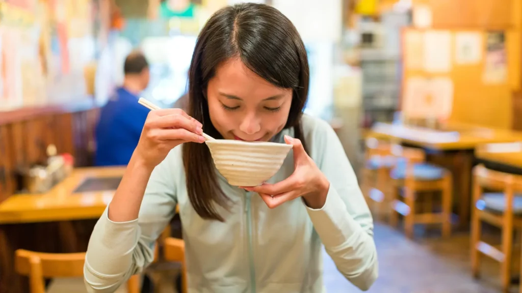 A woman enjoying a bowl of rice at a restaurant, savoring the flavors of her meal.