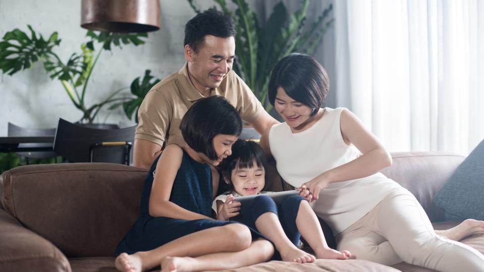 Family happily gathered on couch, using tablet computer together.