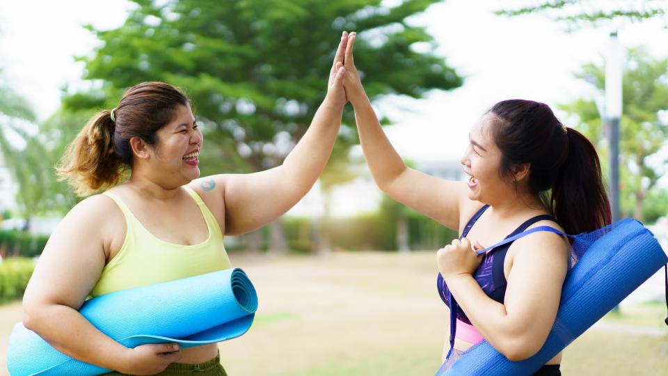 Two women high-fiving with yoga mats in hand.