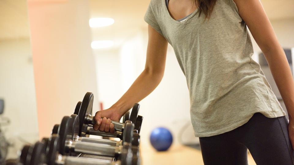 A woman confidently holds a dumbbell in a well-equipped gym, showcasing her dedication to fitness and strength training.