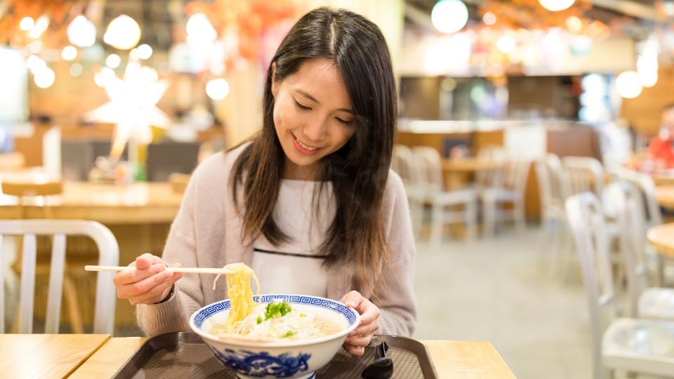A woman enjoying noodles at a restaurant, savoring the delicious flavors of her meal.