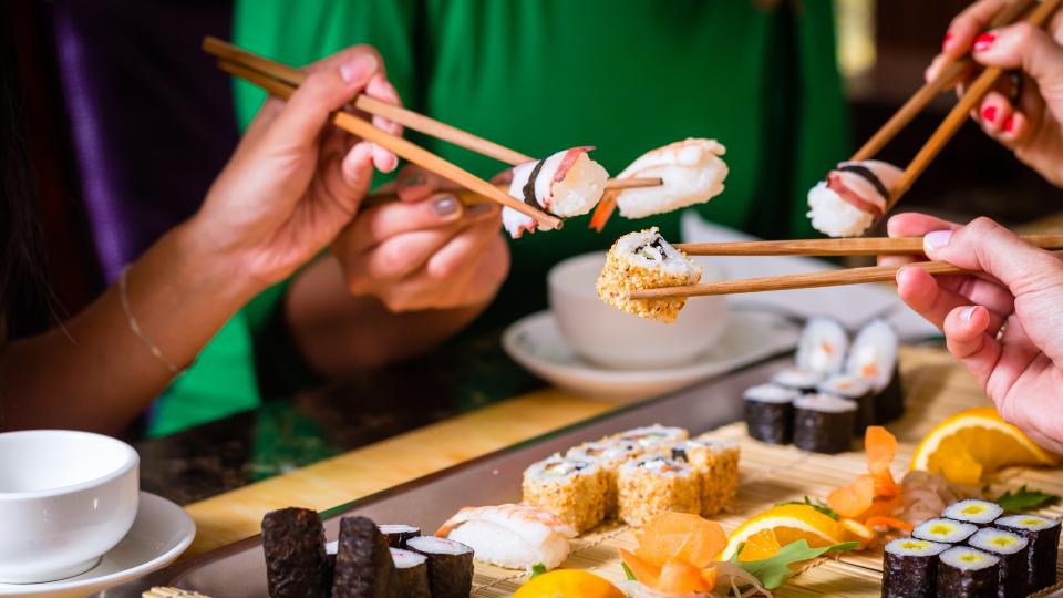 Group of people enjoying sushi together using chopsticks.