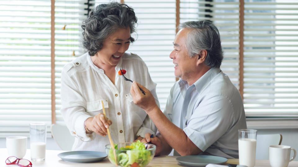 An elderly couple enjoying a meal together at a table, savoring a healthy salad.