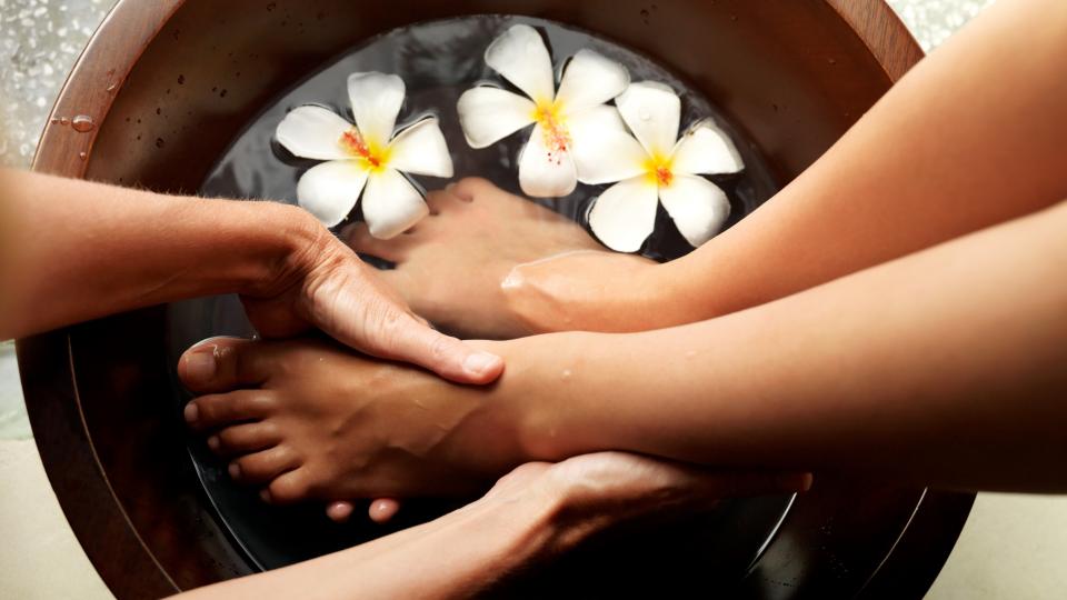 Person's feet being washed in a bowl with flowers, a relaxing spa treatment.