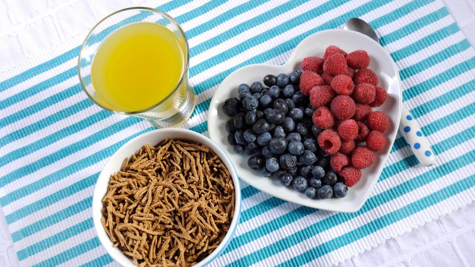 Assorted berries, cereal, and juice on a blue and white striped table.