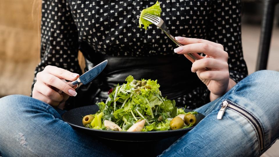 Woman eating salad with fork and knife.