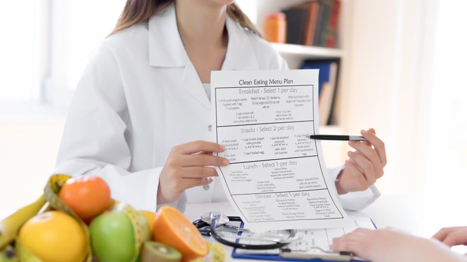 A woman in a lab coat holding a paper with a list of foods.
