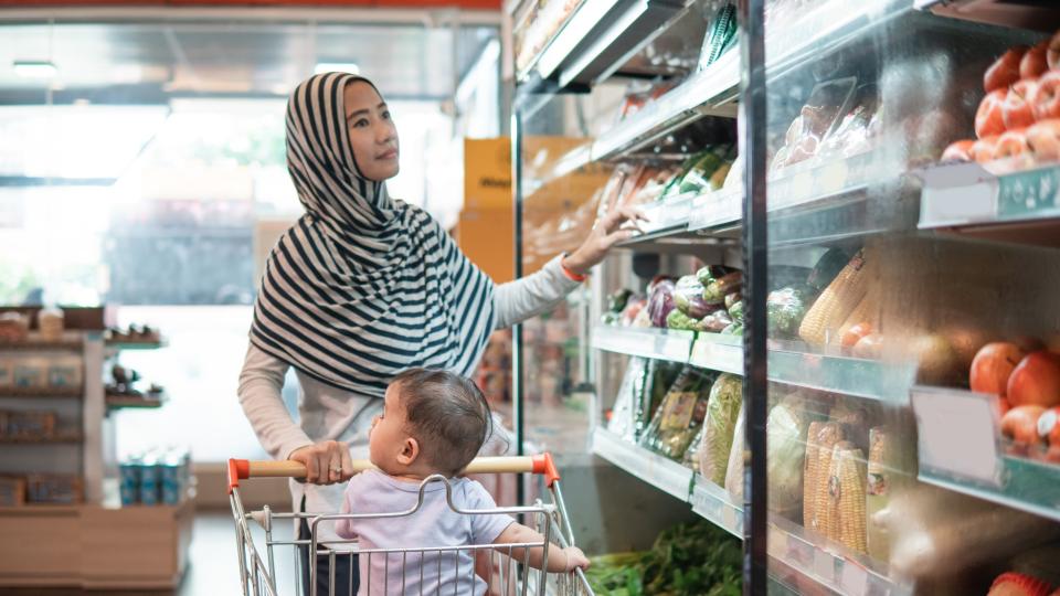 Mother shopping with baby in grocery store.