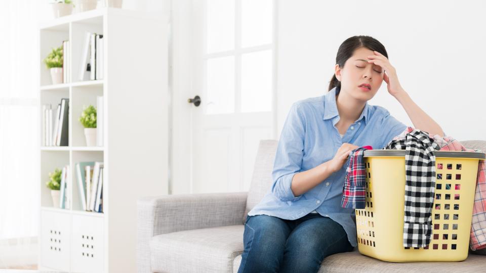A woman sitting on a couch holding a basket of clothes.