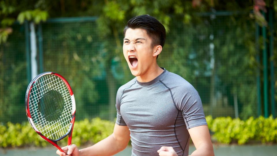 A young man confidently holds a tennis racket, ready to play. His focus and determination are evident in his posture and grip.