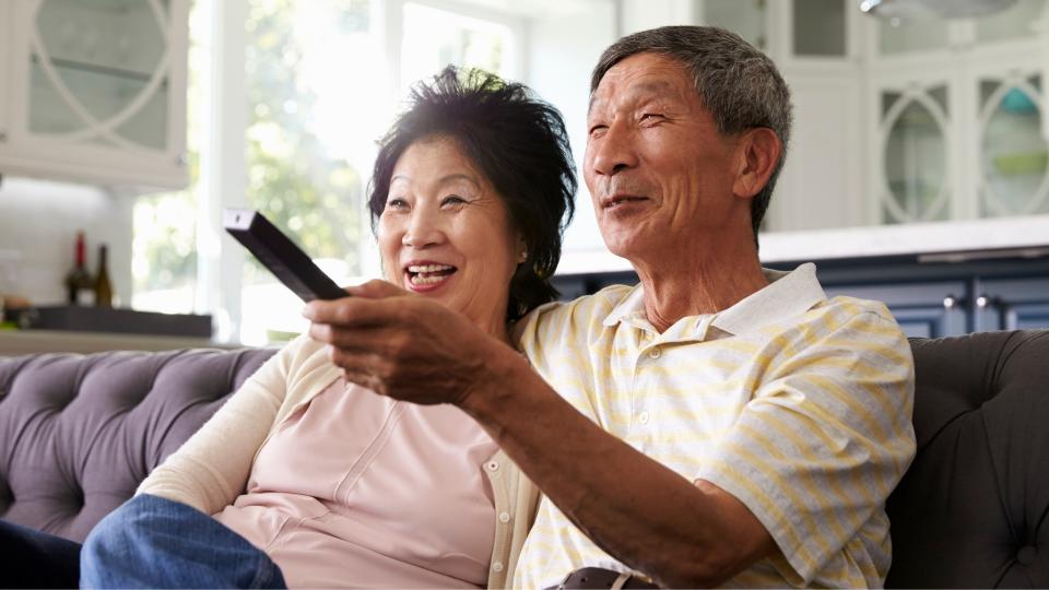 An elderly couple enjoying their time together on a couch, holding a remote control.