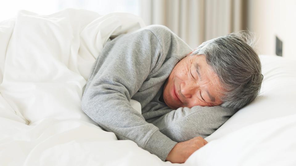 An elderly man peacefully sleeping in bed with his eyes closed.