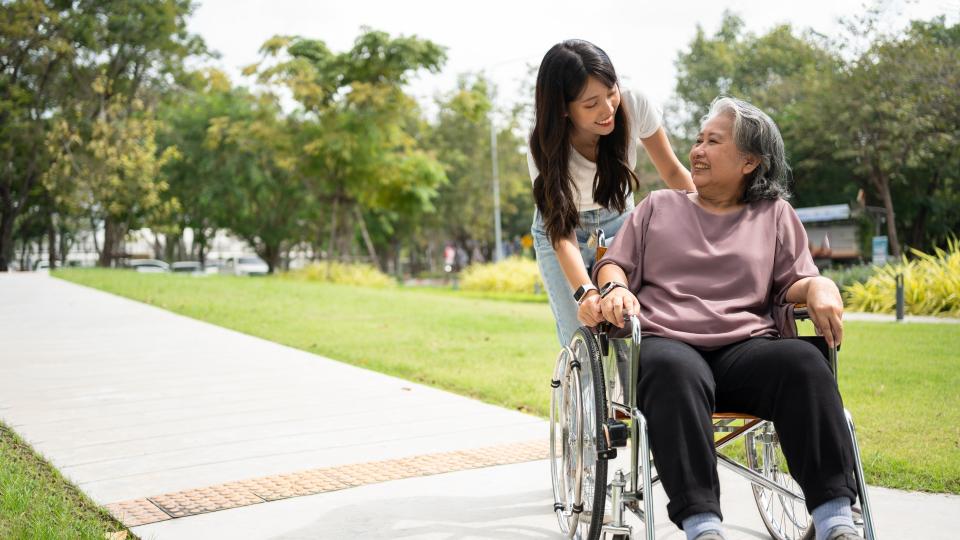 A woman in a wheelchair accompanied by an elderly woman, enjoying a peaceful time together in a park.