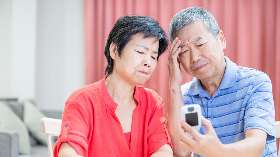 Elderly couple smiling while using smartphone.