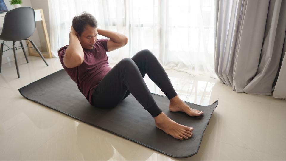 A man sitting cross-legged on a yoga mat in his cozy living room.