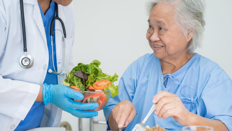 Doctor kindly serves fresh salad to elderly woman at nursing home.