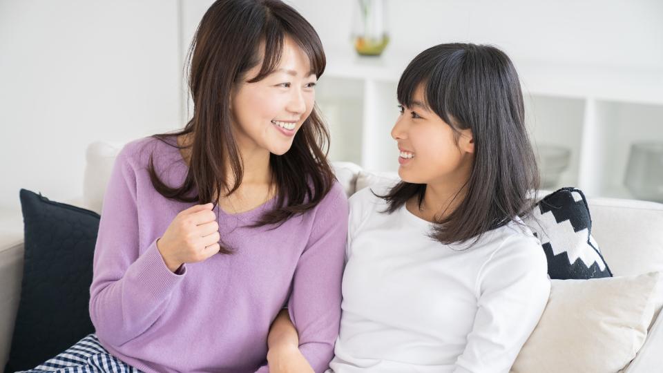 Mother and daughter sitting on a couch, engaged in conversation and smiling.