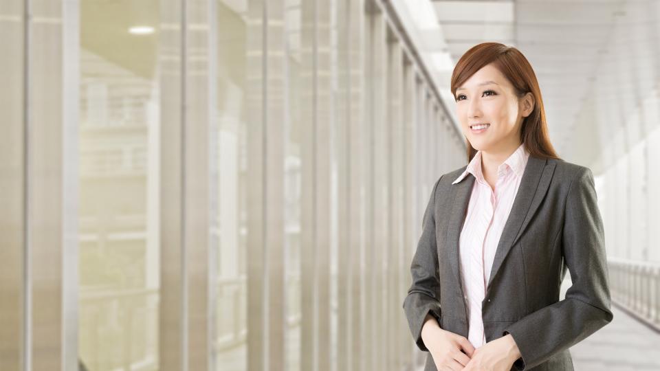 A businesswoman confidently stands in an office hallway, ready to tackle the day's challenges.