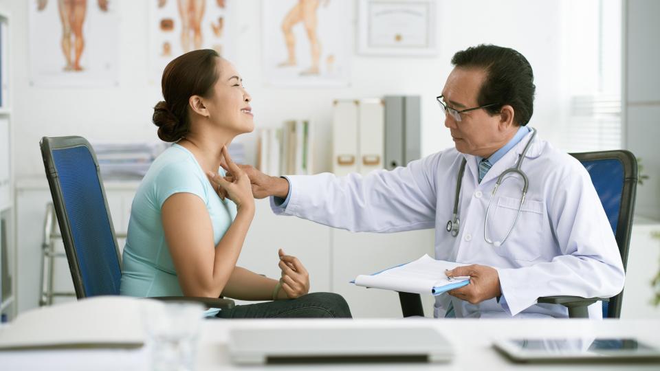 A doctor using a stethoscope to examine a woman's chest in a medical setting.
