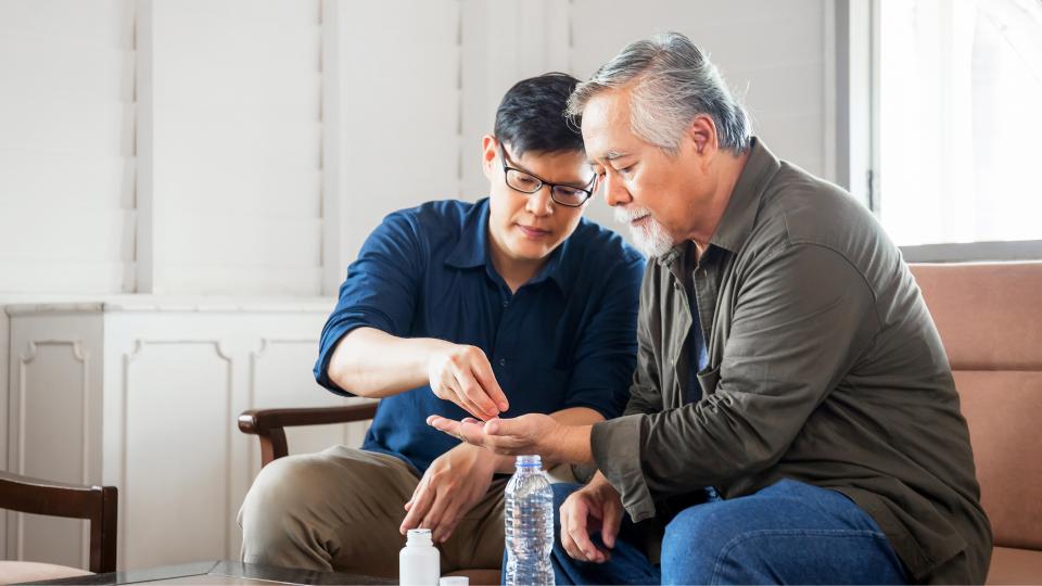 A father and son sitting on a couch looking at a bottle of medicine