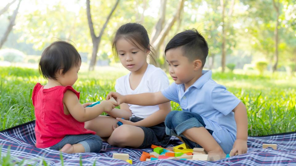 Three kids happily playing with toys on the grass.