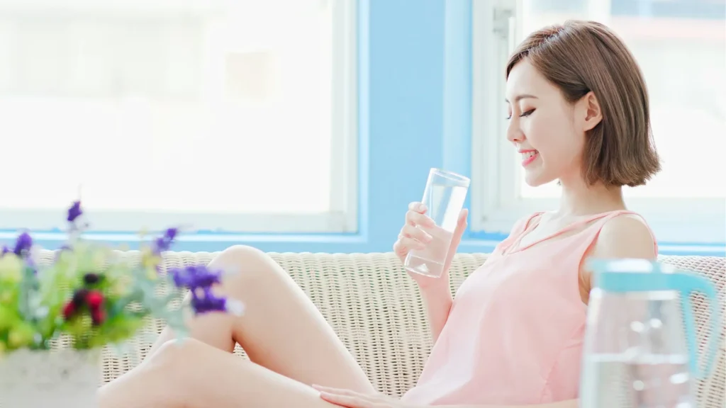 Woman sitting on couch, drinking water.
