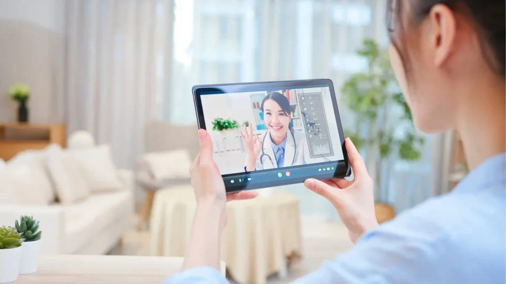 A woman holding up a tablet showing a video of a doctor. Stay connected with healthcare professionals through technology.