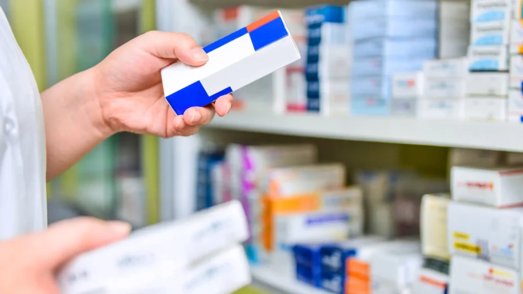 Pharmacist holding a box of medicine in a pharmacy.