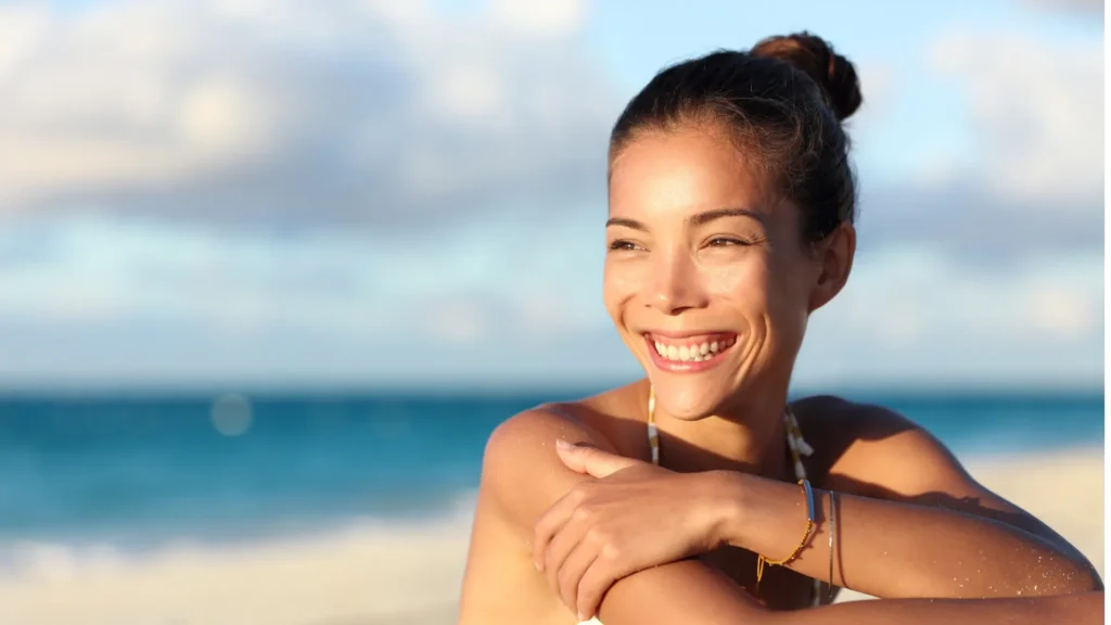 A woman sitting on the beach, smiling brightly.