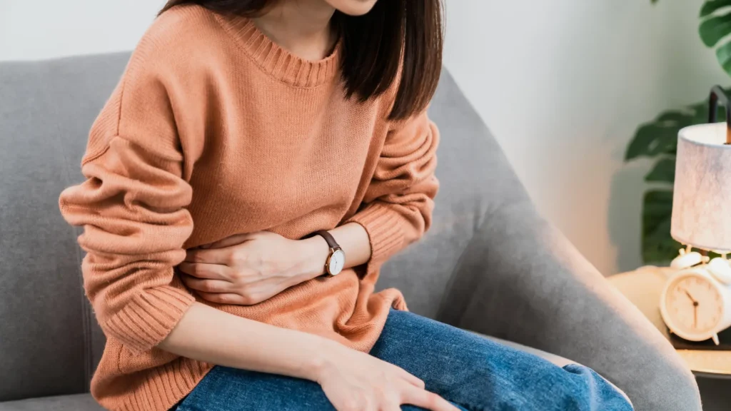 A woman sitting on a couch, clutching her stomach in pain.