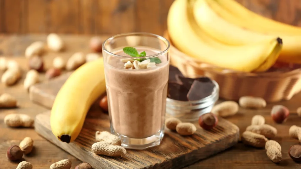 A glass of chocolate shake topped with sliced bananas and crushed nuts.