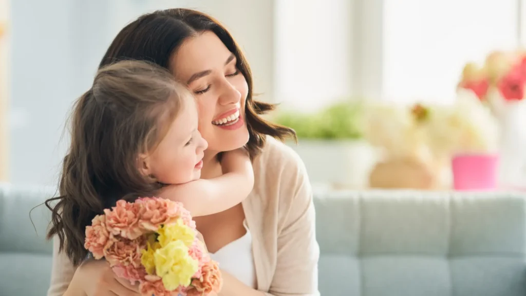 A woman tenderly holds a child in her arms while clutching a bouquet of vibrant flowers.