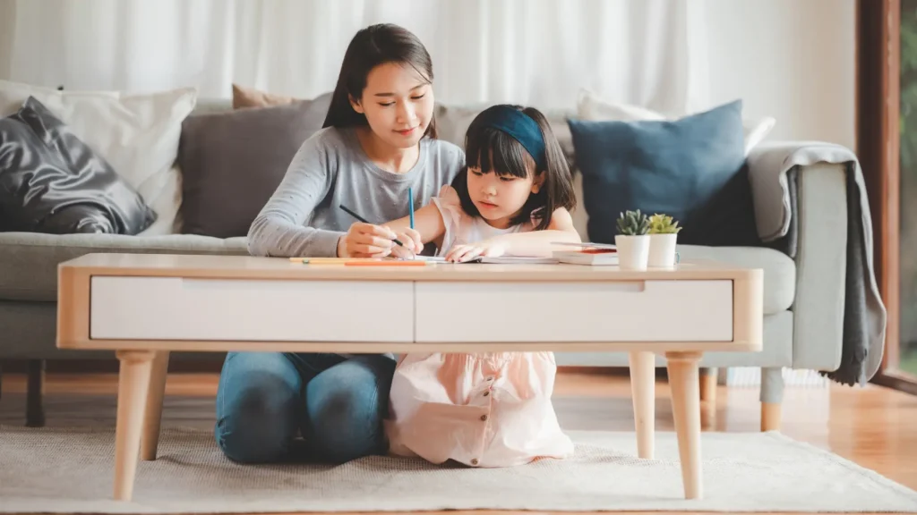 A mother and her daughter sitting on the floor, engaged in writing activities together. How to Build Confidence in a Sensitive Child