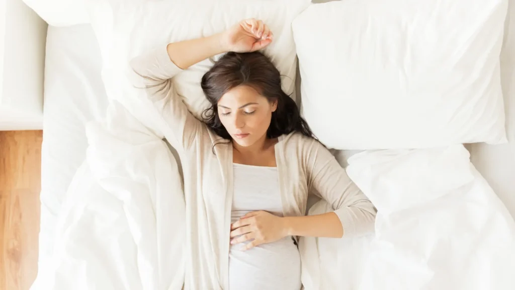 A pregnant woman peacefully laying in bed with her hands lovingly placed on her growing stomach.