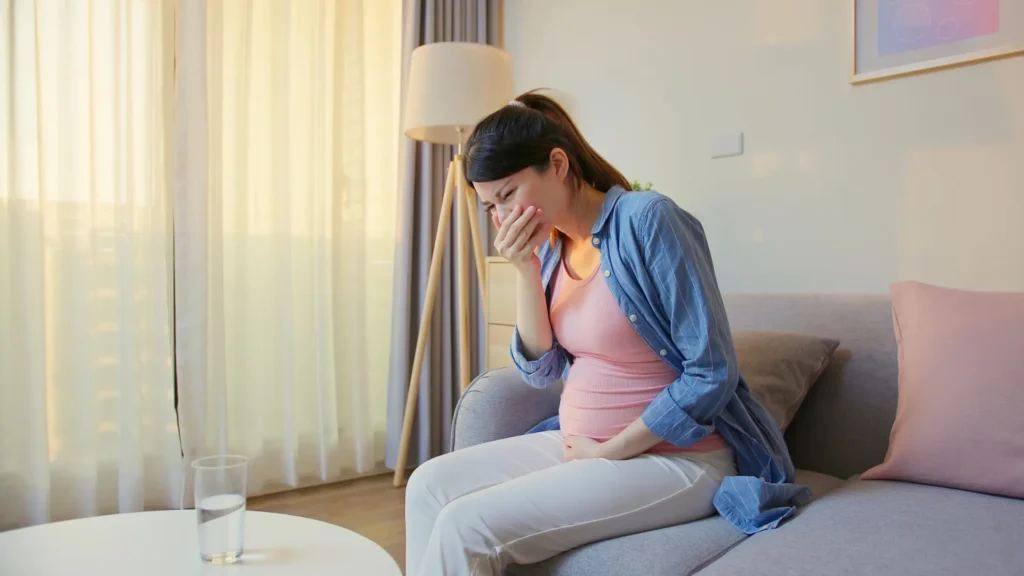 A pregnant woman sitting comfortably on a couch, cradling her belly with a serene expression.