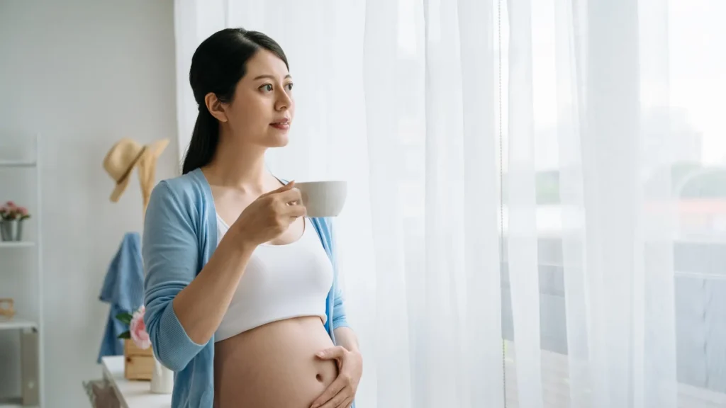 A pregnant woman gently cradling a cup of coffee in her hands, enjoying a warm beverage.