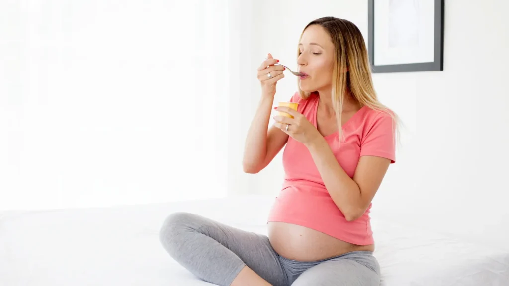 A pregnant woman sitting on a bed, enjoying a banana. Postpartum Diarrhea Home remedies