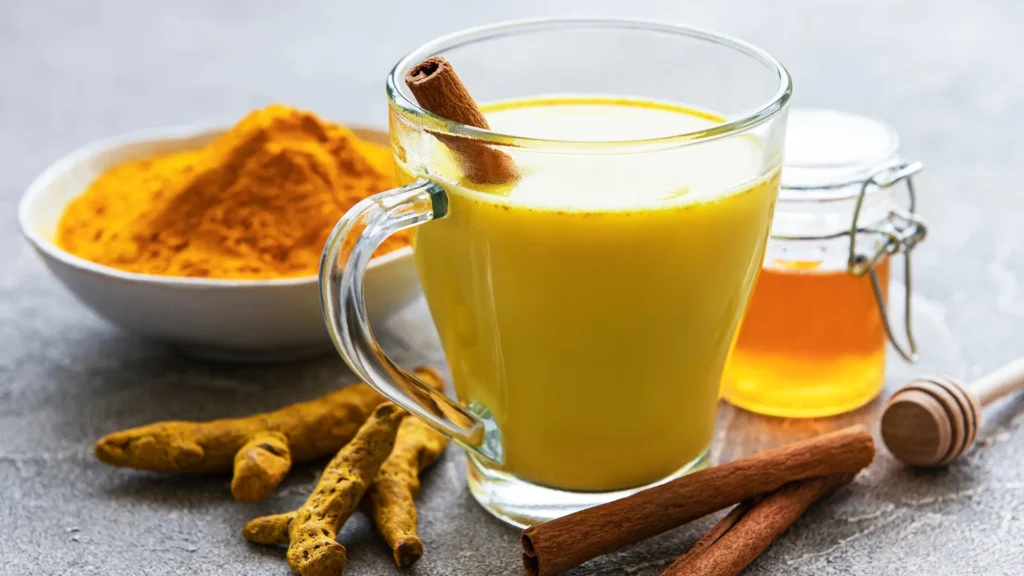 A glass filled with tumeric and honey, garnished with cinnamon sticks.