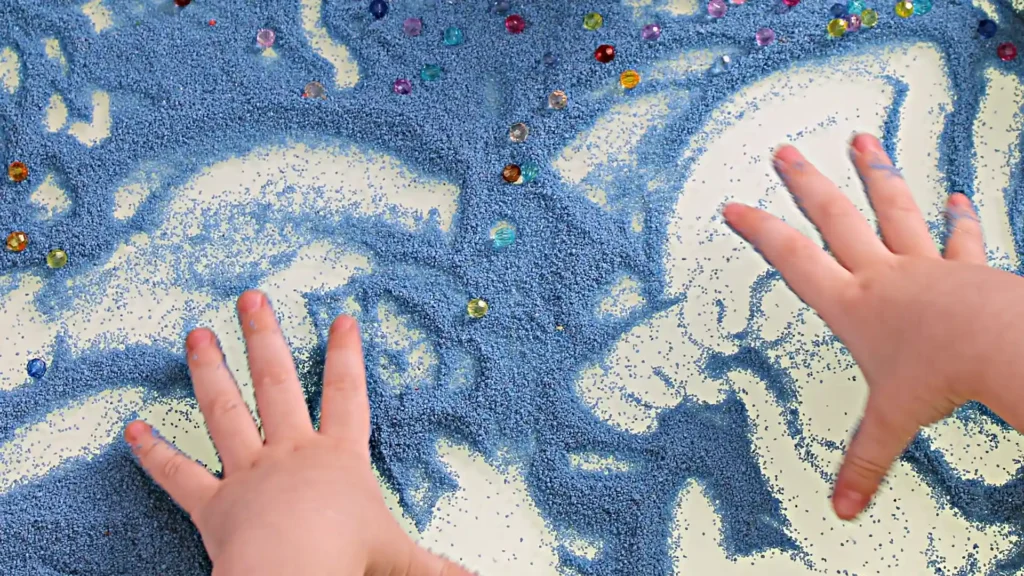 A child's hands playing in the sand, feeling the texture and enjoying the Sensory Stimulation experience.
