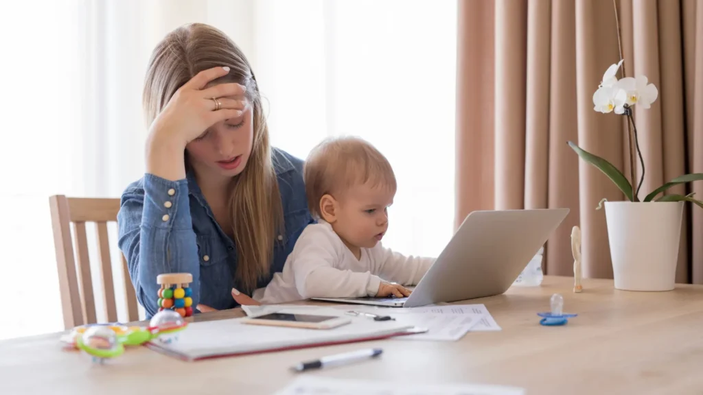 How to Manage Postpartum Fatigue. 1. A woman and a baby sitting at a table with a laptop.