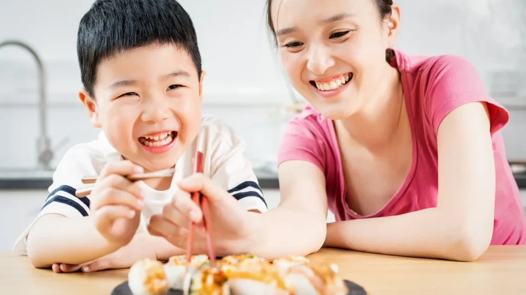 A woman and a boy happily enjoy sushi, smiling as they savor the delicious flavors.