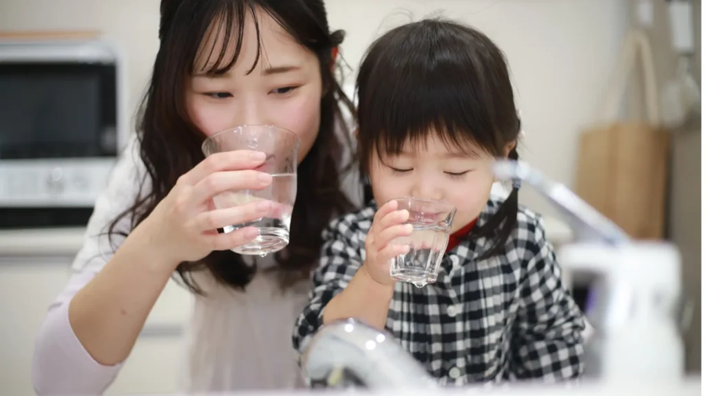 A woman and child hydrating themselves by drinking water from a glass.