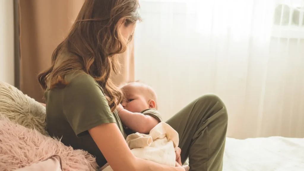 A woman in green pajamas cradling her baby in her arms.